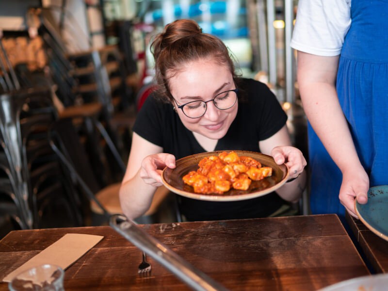 Smiling woman with her eyes closed holds a plate of gnocchi 